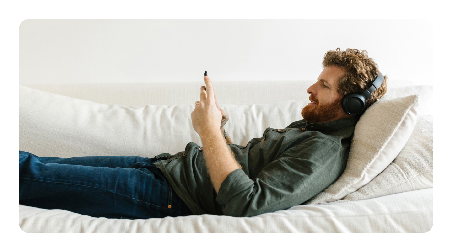 Ein Mann liegt auf einem Sofa und trägt Kopfhörer, während er sein Smartphone bedient.